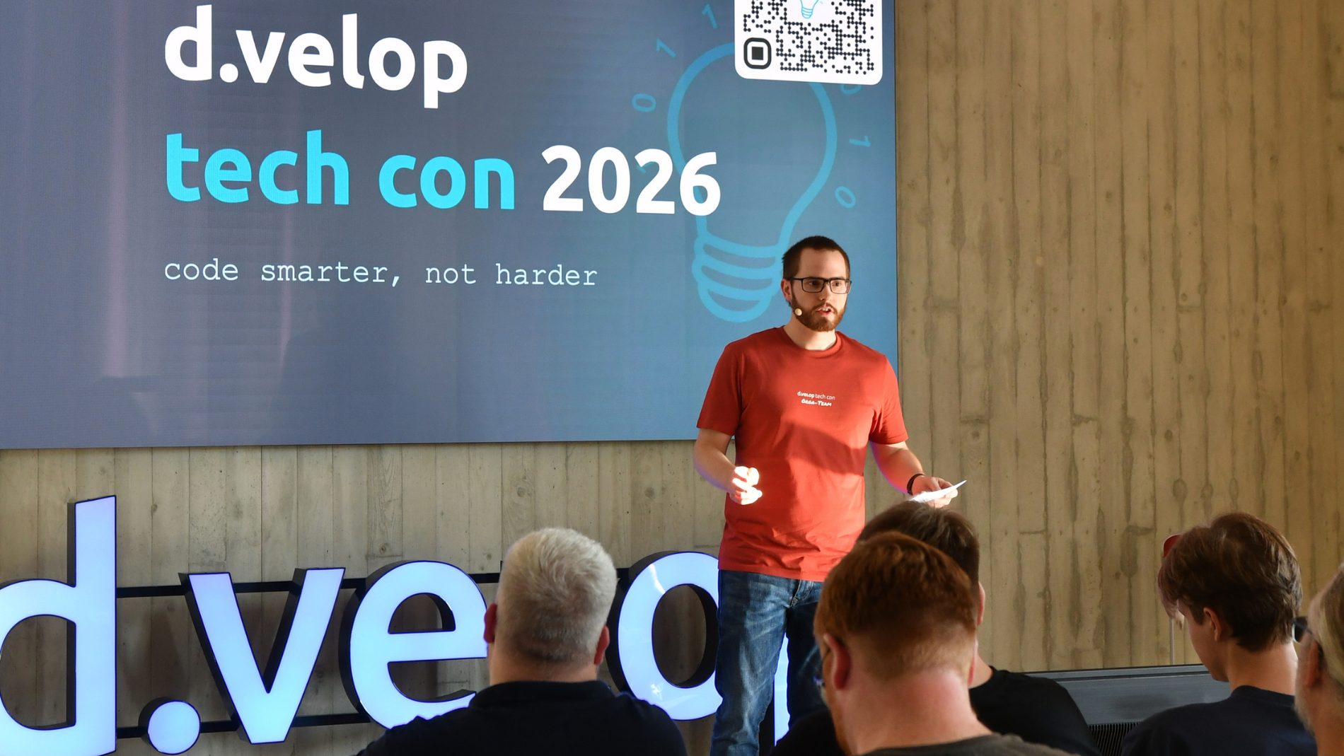 Moderator auf der Bühne der d.velop tech con 2026 vor dem Motto „code smarter, not harder“